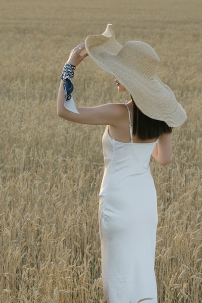 During the day, wearing a white sleeveless dress woman standing in the brown grass
